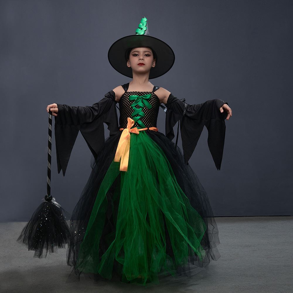 Girl wearing a green and black witch dress with an orange waist ribbon, pointed hat, and bat-wing sleeves while holding a decorative broom.