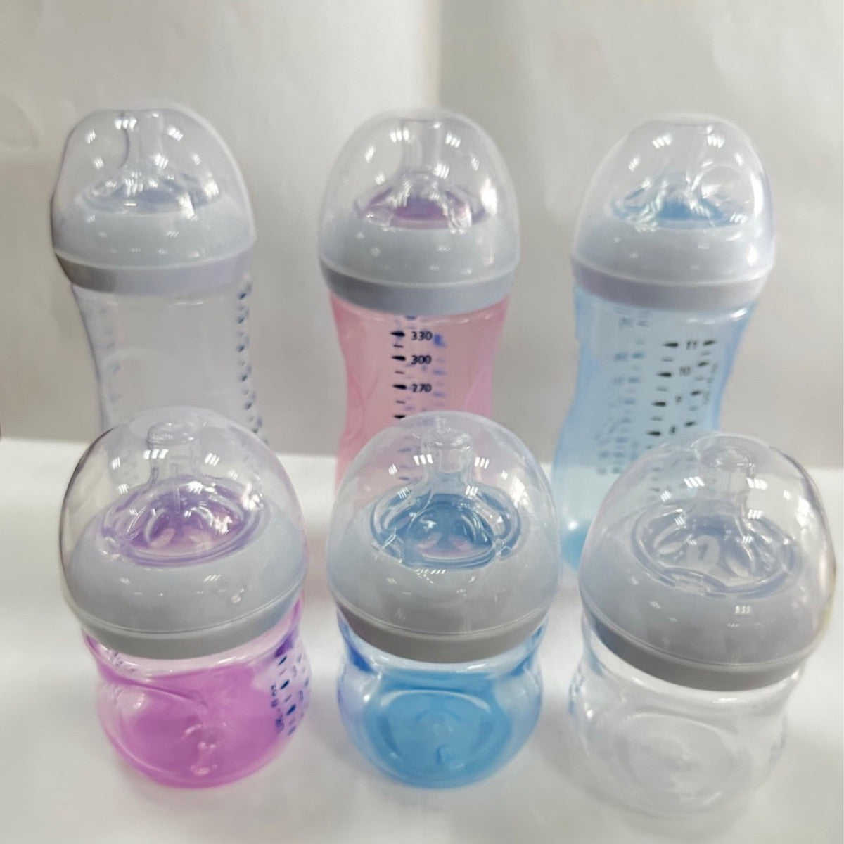 Petal nipple baby feeding bottle without handles, available in transparent, pink-purple and light blue.