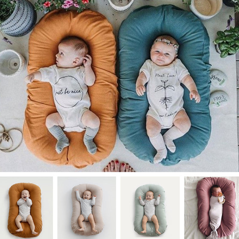 Portable cotton baby nest cushion measuring 75 × 45 cm, with raised padded sides and multiple colour options.