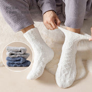 Person wearing white ultra-soft coral velvet thermal socks while relaxing at home, with folded grey and blue pairs shown nearby