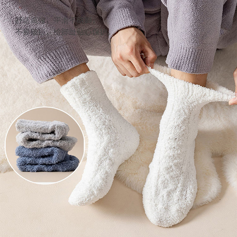 Person wearing white ultra-soft coral velvet thermal socks while relaxing at home, with folded grey and blue pairs shown nearby