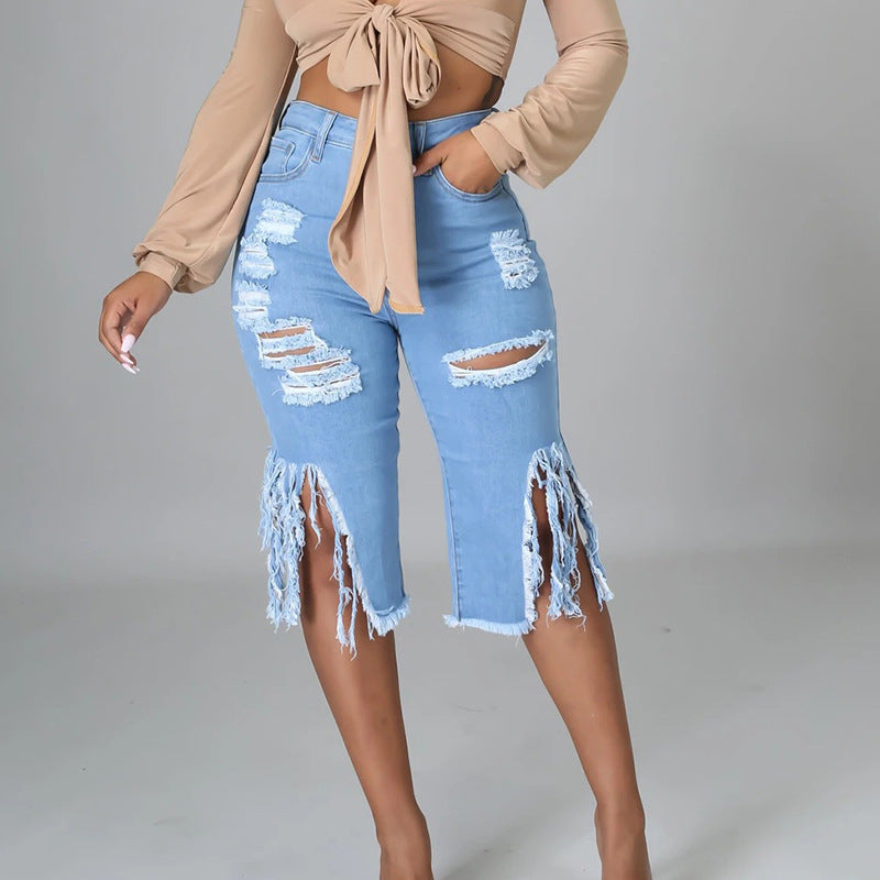 Women’s light-wash knee-length denim shorts with ripped thigh panels, dramatic frayed knee openings and raw fringed hems